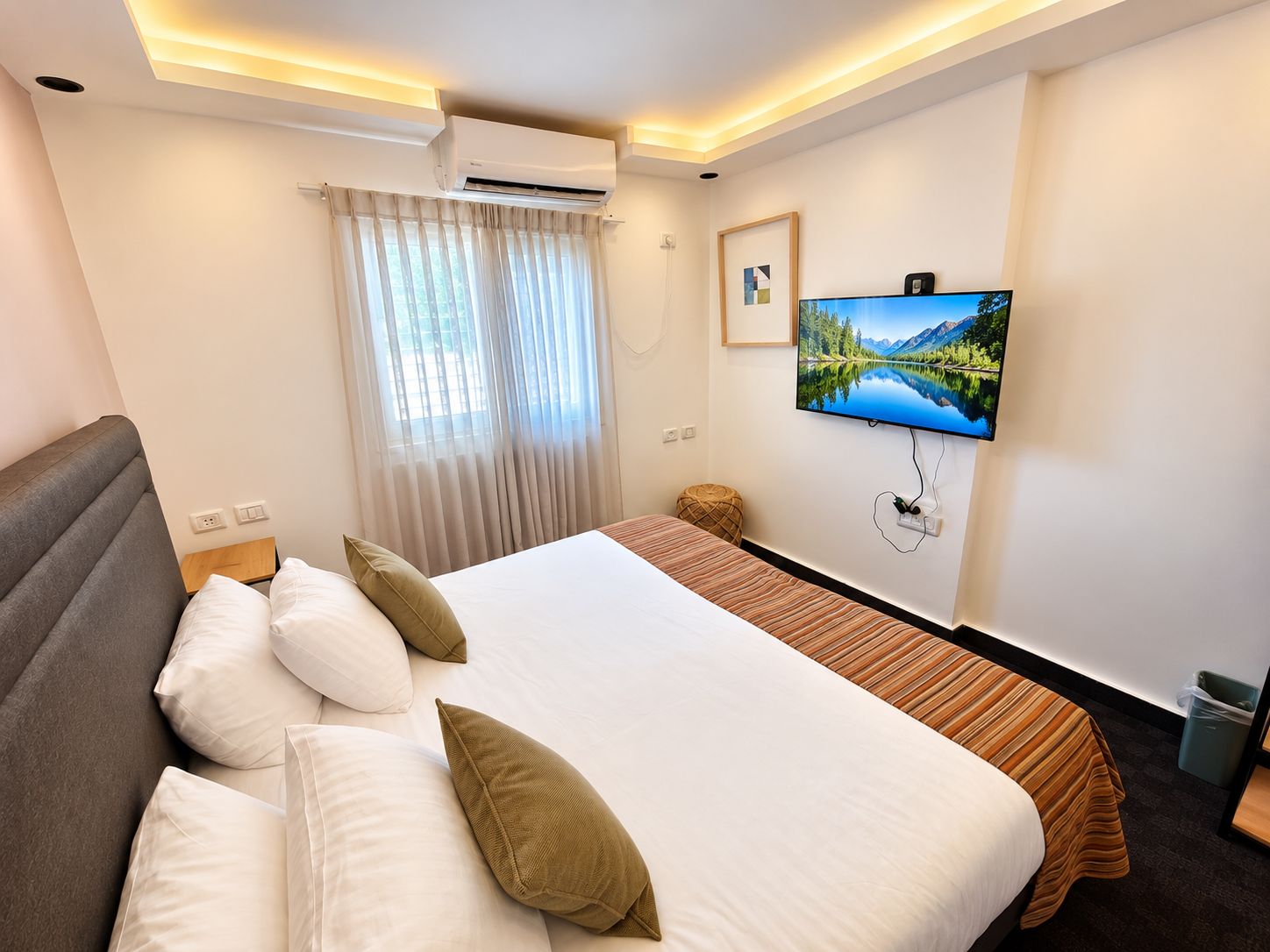 Une chambre d’hôtel équipée d’un lit, d’un téléviseur fixé au mur, d’une fenêtre avec des rideaux et d’un appareil de climatisation.