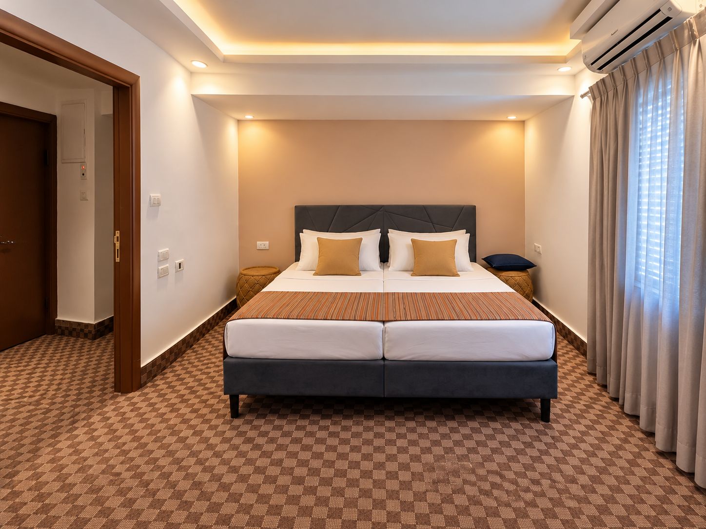 Une chambre d’hôtel avec un grand lit, une table de chevet, un climatiseur fixé au mur et une fenêtre avec des rideaux.