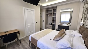 A hotel room with a bed, bedside table, desk, chair, wardrobe, and a mirror.