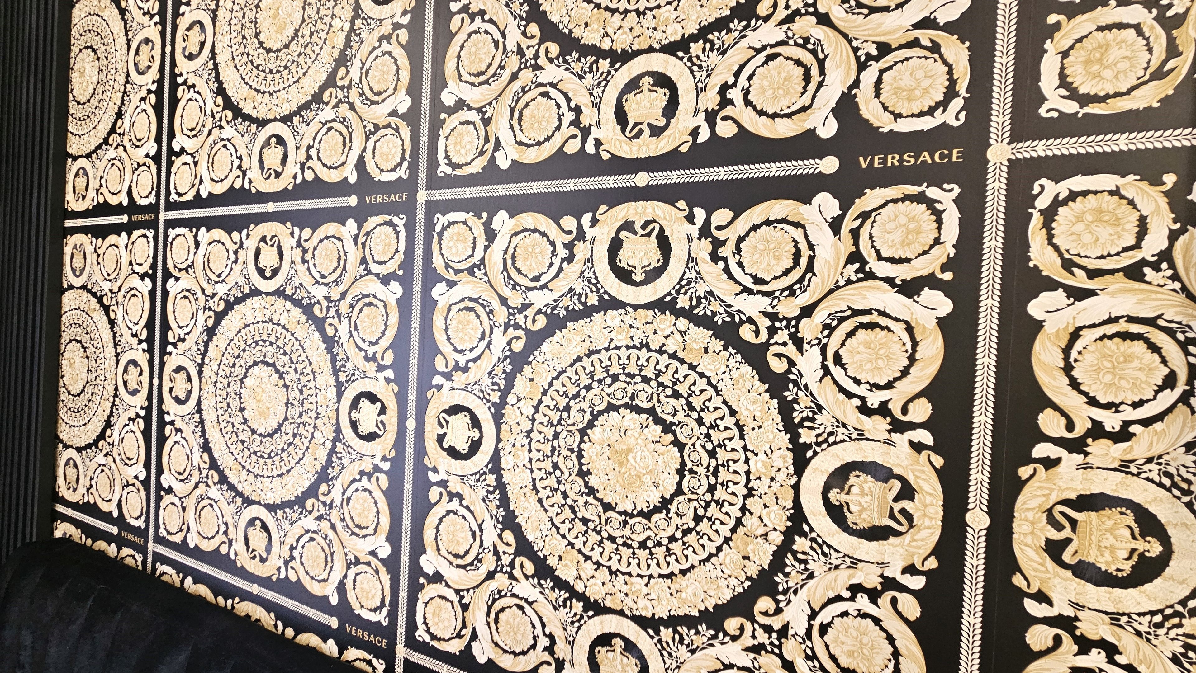 A wall with intricate gold patterns and the word 'VERSACE' repeated across it.