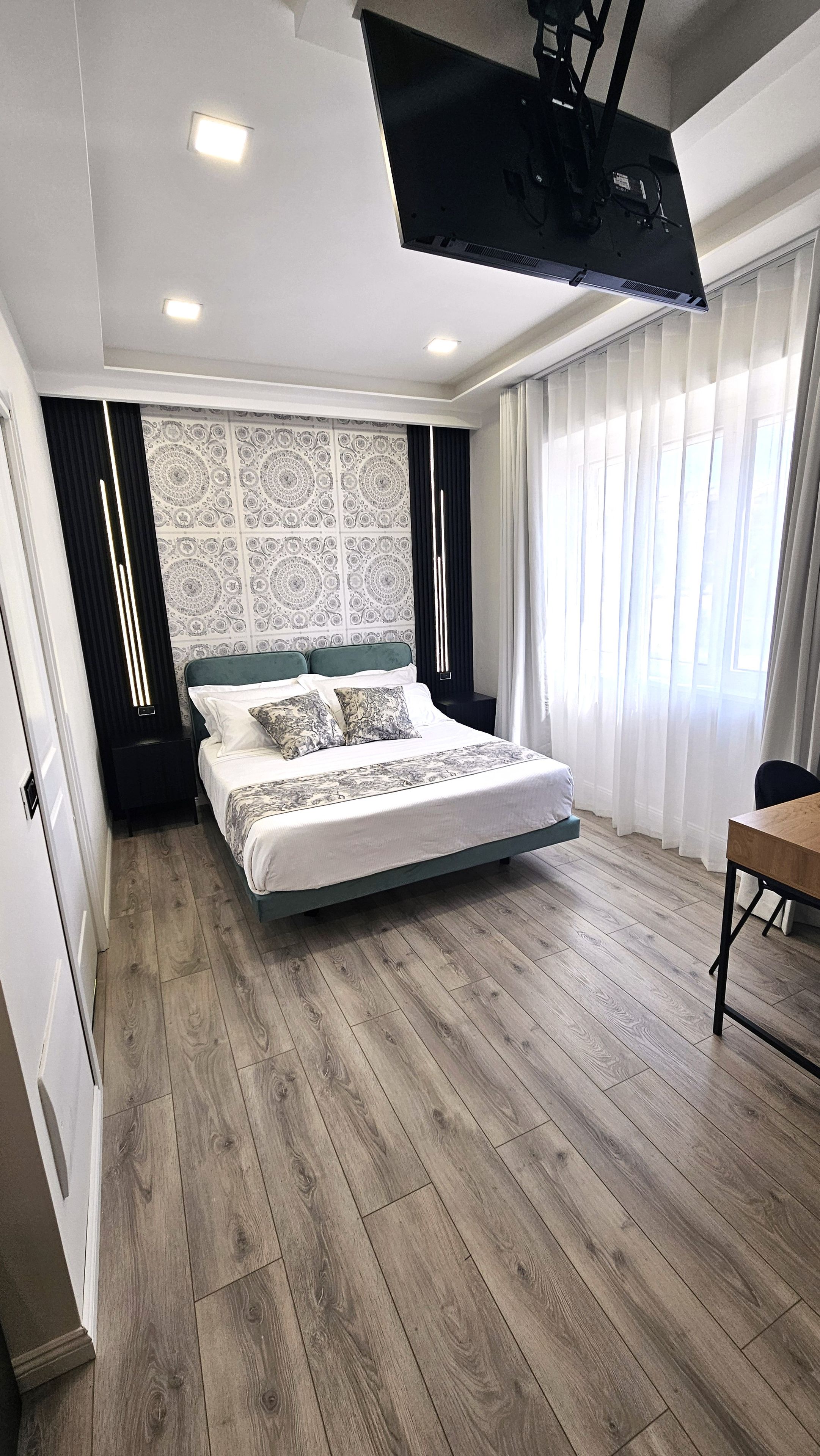 A modern bedroom with a bed, a flat-screen TV mounted on the ceiling, and a wooden floor.