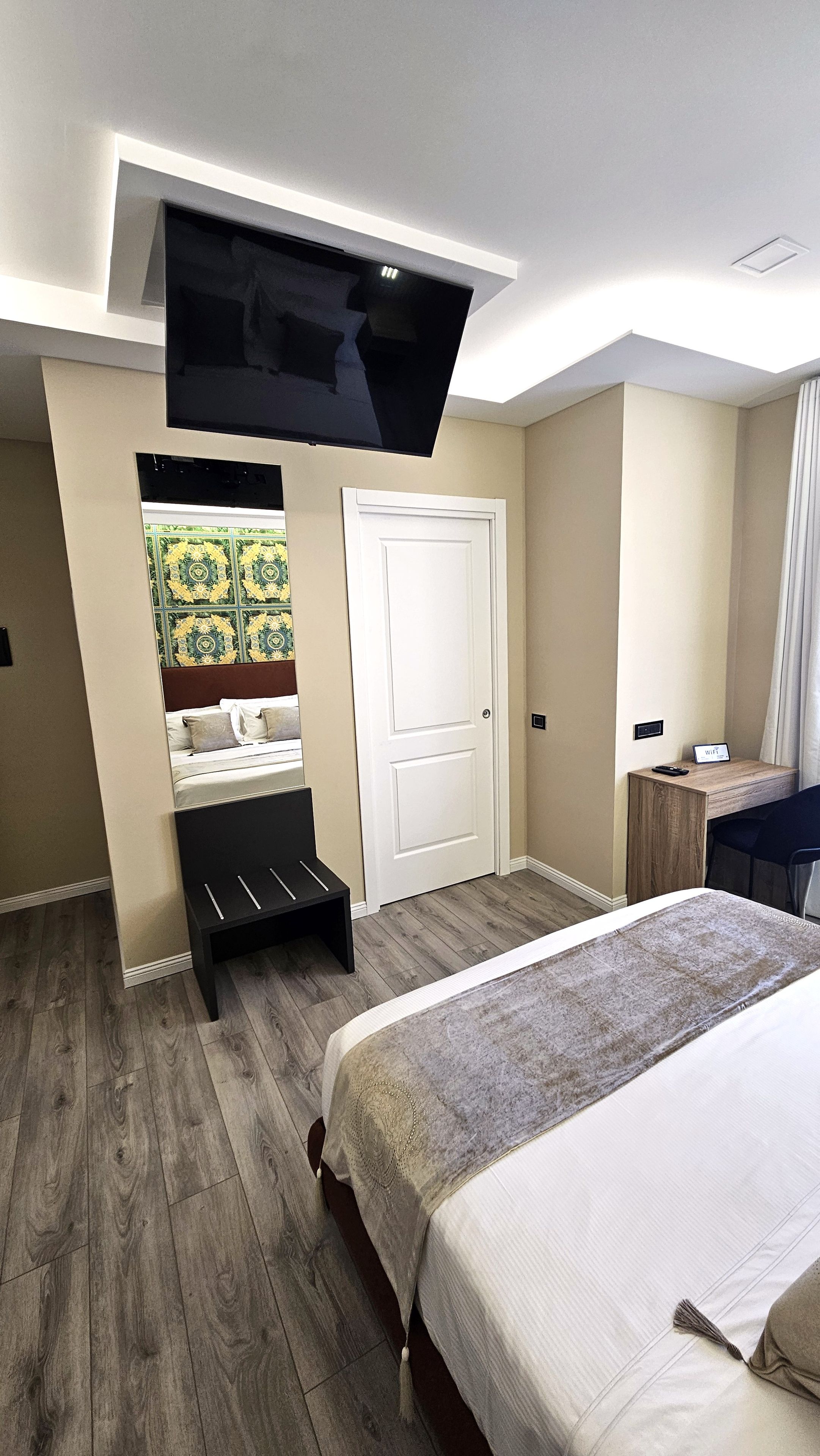 A hotel room with a bed, a desk, a TV mounted on the wall, and a door.
