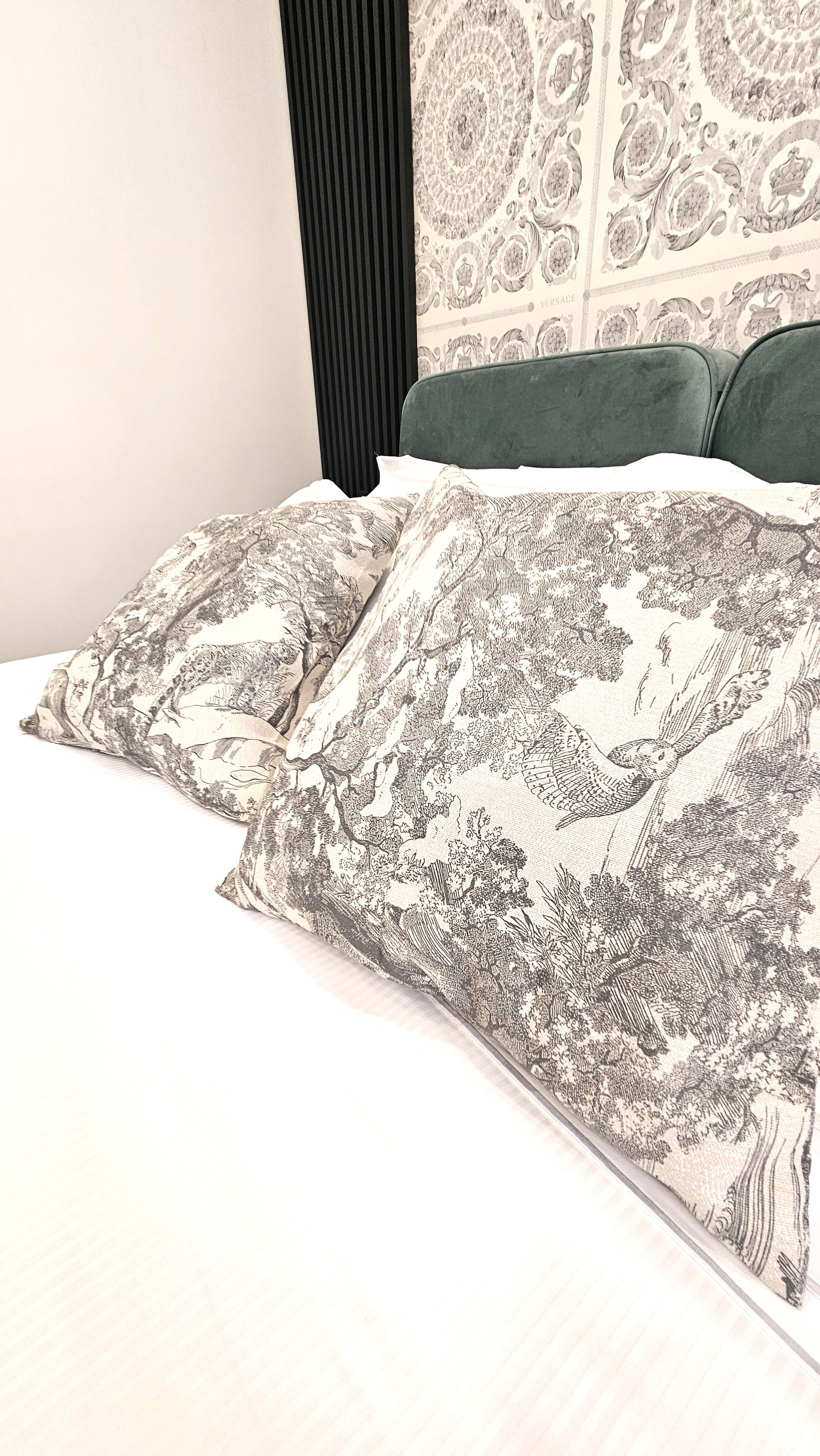 Una cama con almohadas estampadas y un cabecero oscuro frente a una pared con un diseño detallado.
