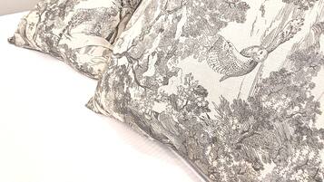 Una cama con almohadas estampadas y un cabecero oscuro frente a una pared con un diseño detallado.