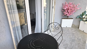 Um pátio com uma mesa redonda e cadeiras, uma porta de vidro deslizante e plantas em vasos.