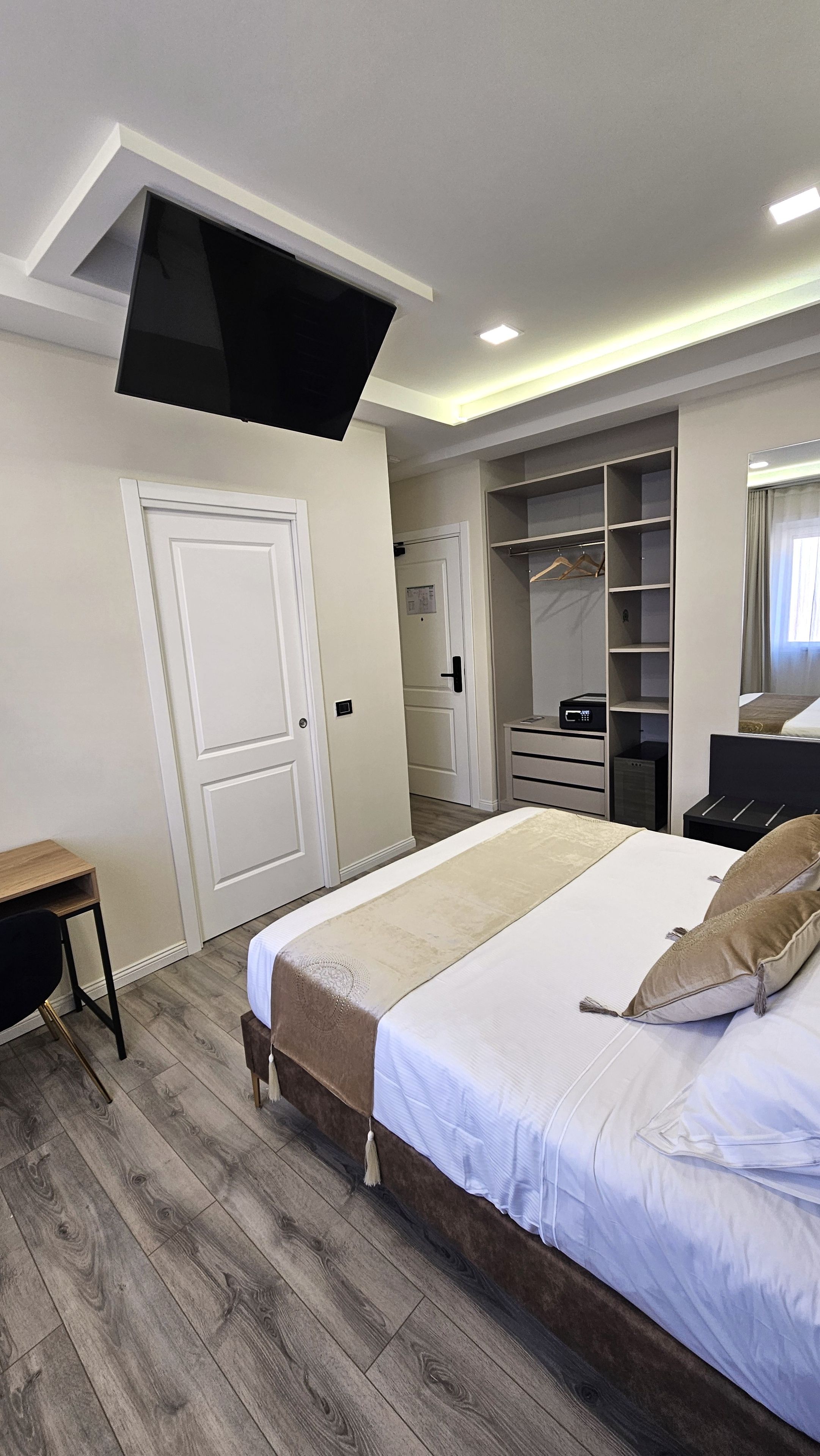 A bedroom with a bed, a TV mounted on the ceiling, a wardrobe, and a desk.