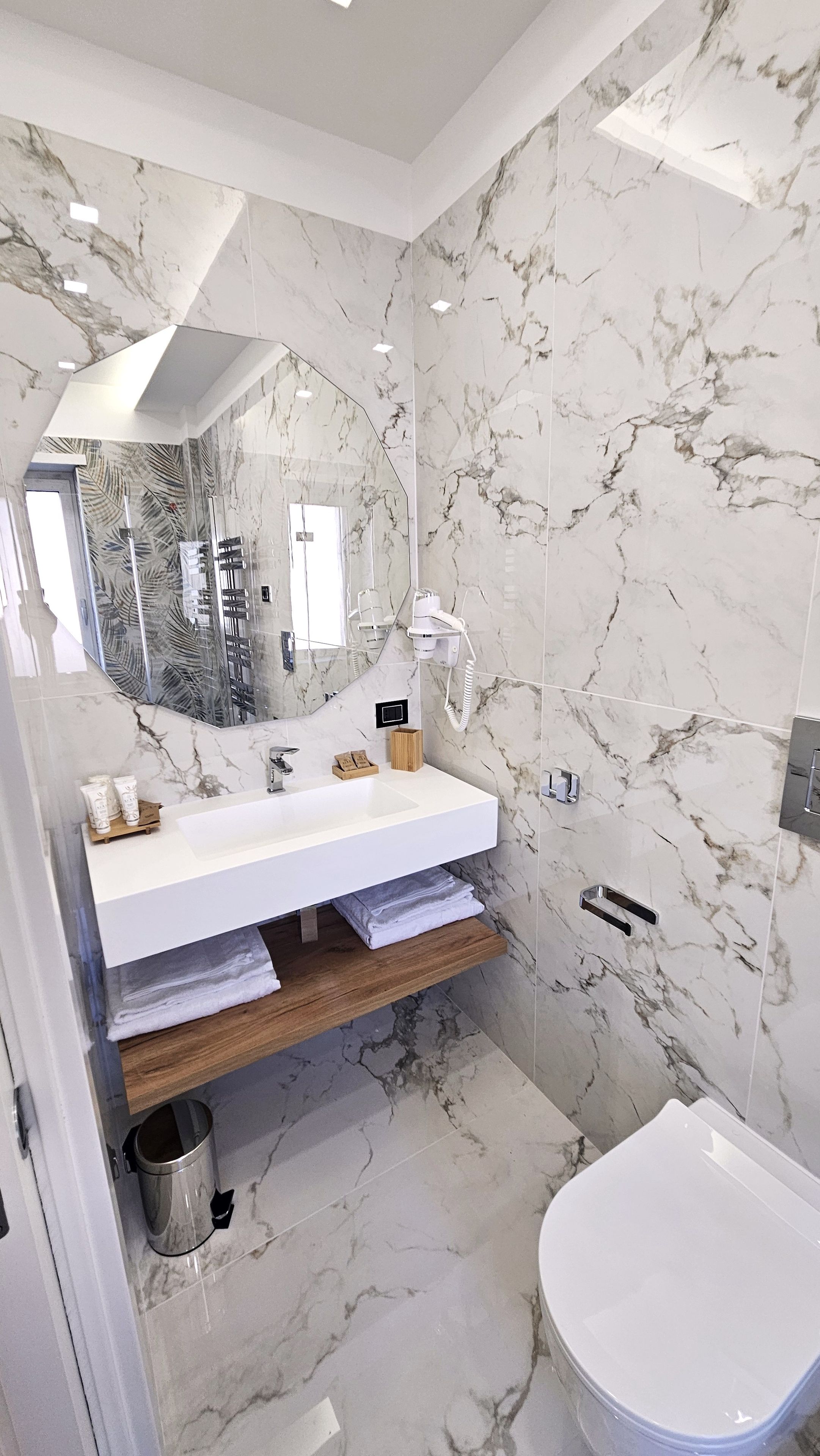 Un bagno moderno con rivestimento in marmo, un lavandino bianco e un water.