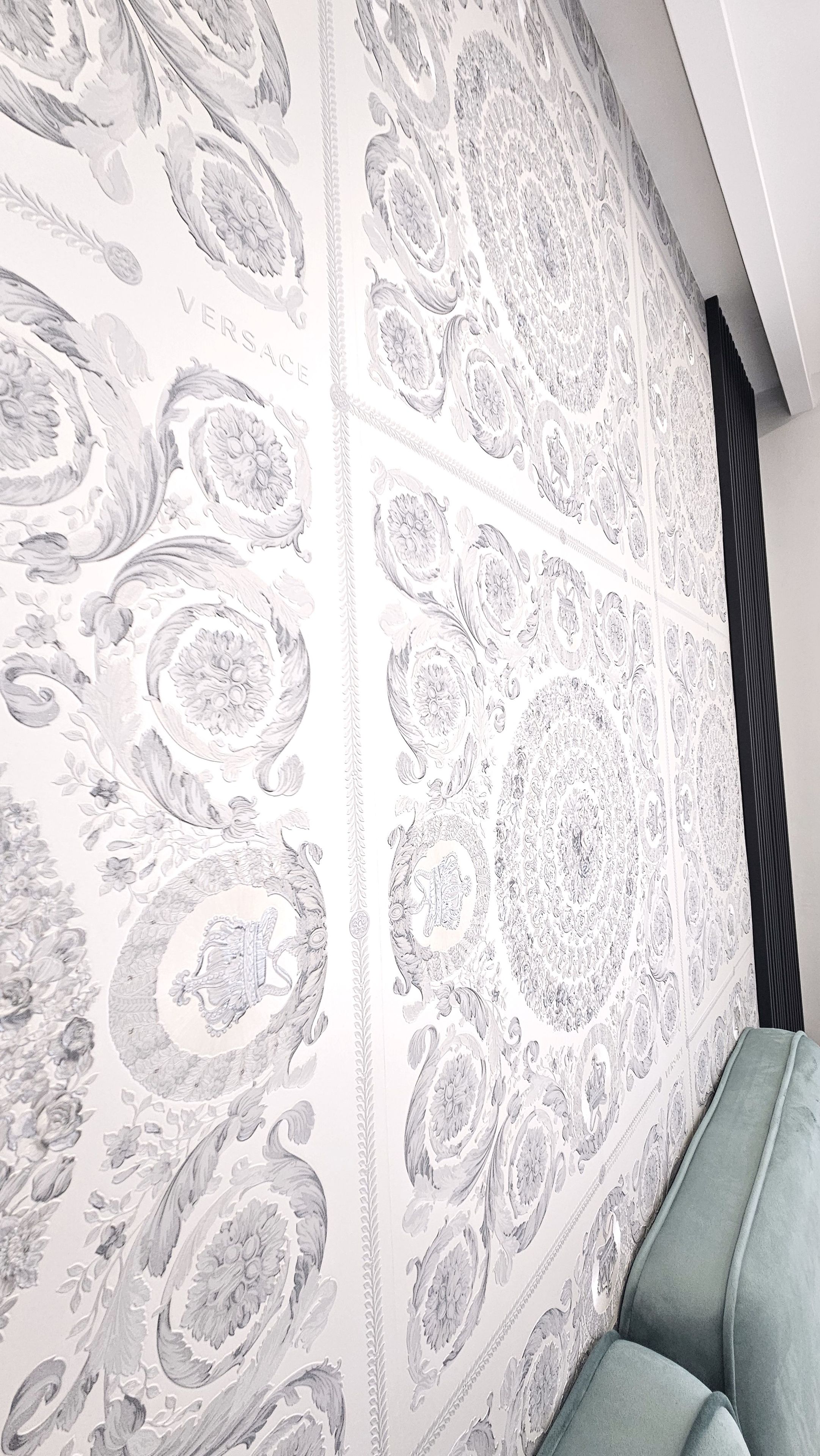 Pared con intrincados diseños florales y estampados paisley, un sofá tapizado en verde y un elemento vertical oscuro a la derecha.