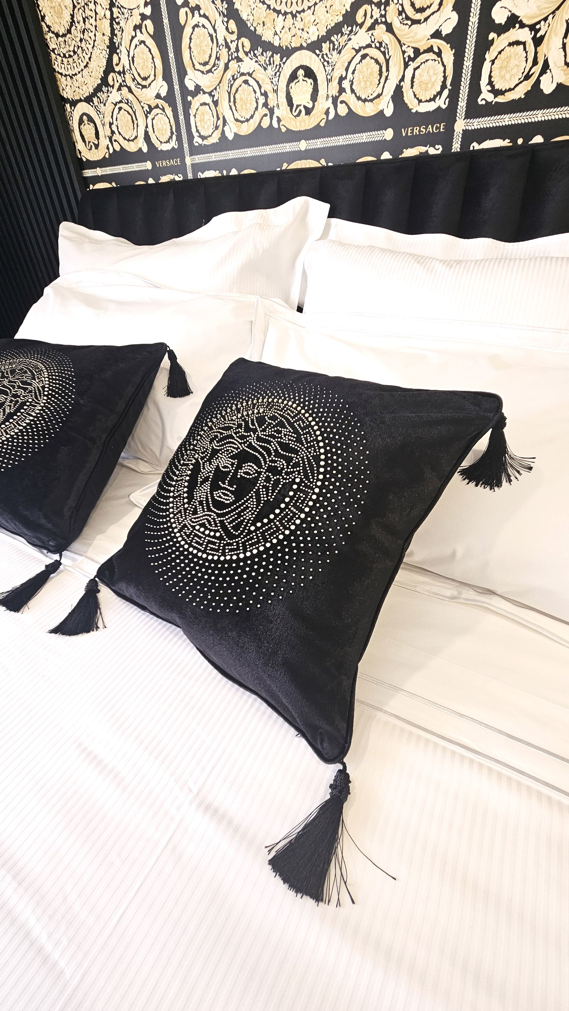 A bed with white bedding and black pillows with intricate white patterns.