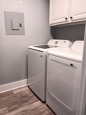 A laundry room with two front-loading washing machines and a dryer, white cabinets above, and a light switch on the wall. -  Lake Home, Private Pier, Smoker/Grill included. Sunrises in your backyard. (Lake Waccamaw)