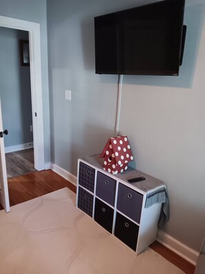 Ett rum med en platt-TV som är monterad på väggen, ett förvaringsskåp med lådor och en dörr som leder till ett annat rum.
