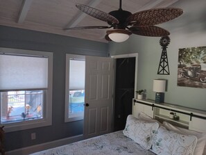 Une chambre à coucher avec un lit, un ventilateur de plafond, une fenêtre et une porte.