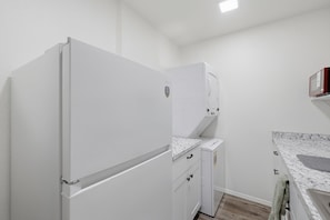 Een kleine keuken met witte apparaten, een marmeren aanrecht en een kastje.