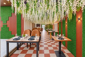 A restaurant with a checkered floor, green walls, and hanging white flowers. Tables are set with plates, glasses, and cutlery. - Classic Hotel Dream Palace (Danapur)