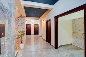 A hotel hallway with marble flooring, a plant, and a digital display. - Classic Hotel Dream Palace (Danapur)