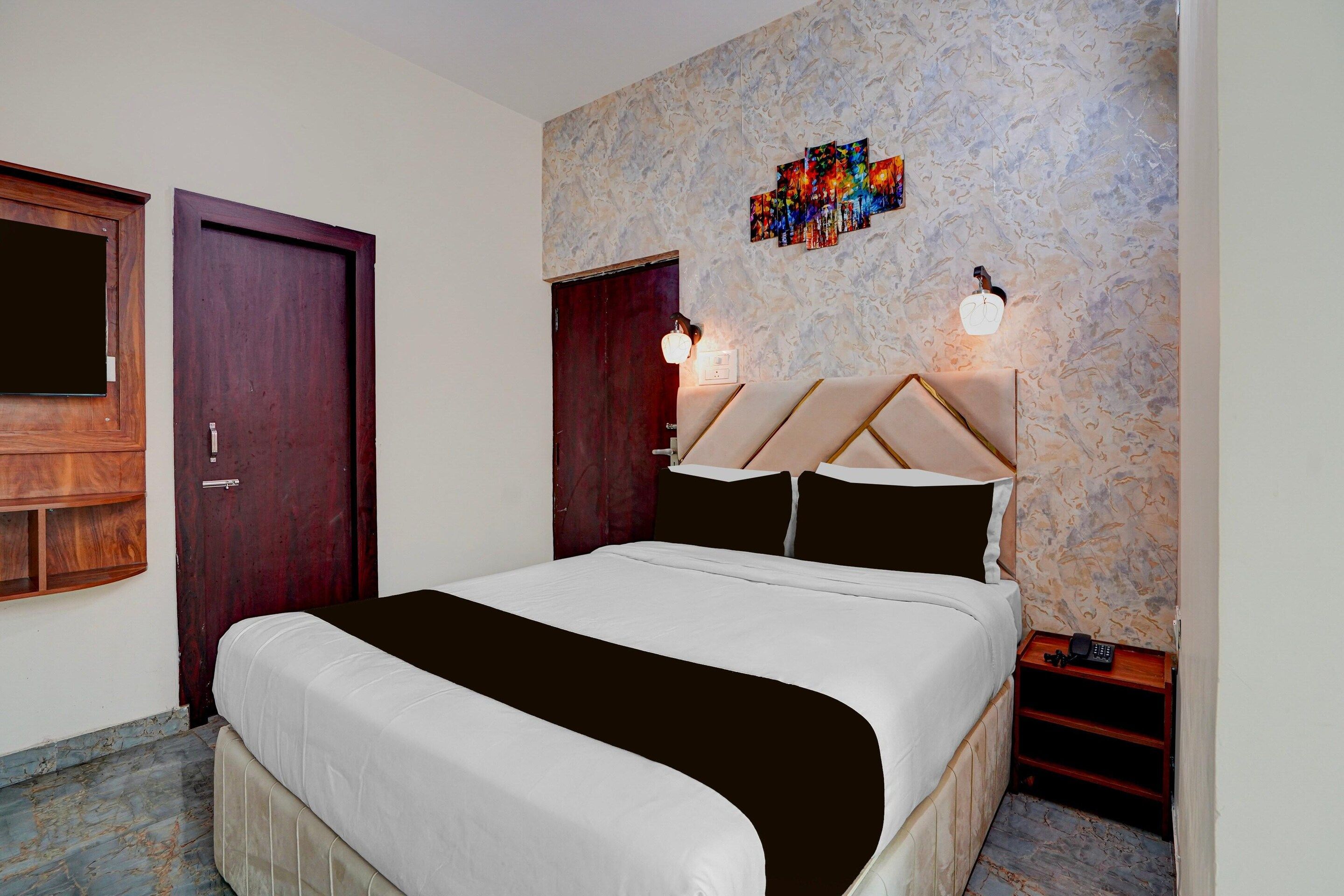 Habitación de hotel con una cama, una puerta de madera, una pared con diseño tipo mármol y una mesita con un teléfono.
