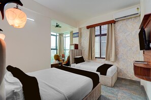 Ein Hotelzimmer mit zwei Betten, einem Schreibtisch mit Stuhl, einer Klimaanlage und Blick auf die Stadt durch die Fenster.