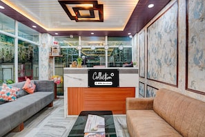 A reception area with a wooden reception desk, two sofas, a coffee table, and a large window with plants. - Classic Hotel Dream Palace (Danapur)