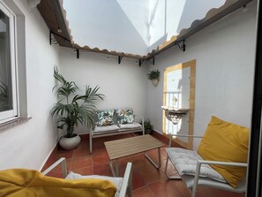 A sunlit patio with a white wall, a wooden bench, a white chair, a yellow cushion, and a potted plant. - Charming Little House (Requena)