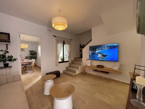 A modern living room with a flat-screen TV, a dining area with a table and chairs, and a staircase leading to another level.