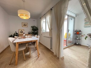 A dining area with a table and chairs, a hanging light fixture, a potted plant, and a window with curtains.