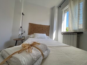 Una cama bien hecha con cabecera, una mesita de noche con lámpara y una ventana con cortinas.