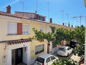 Una calle residencial con hilera de casas, un coche blanco estacionado y un árbol de hojas verdes.