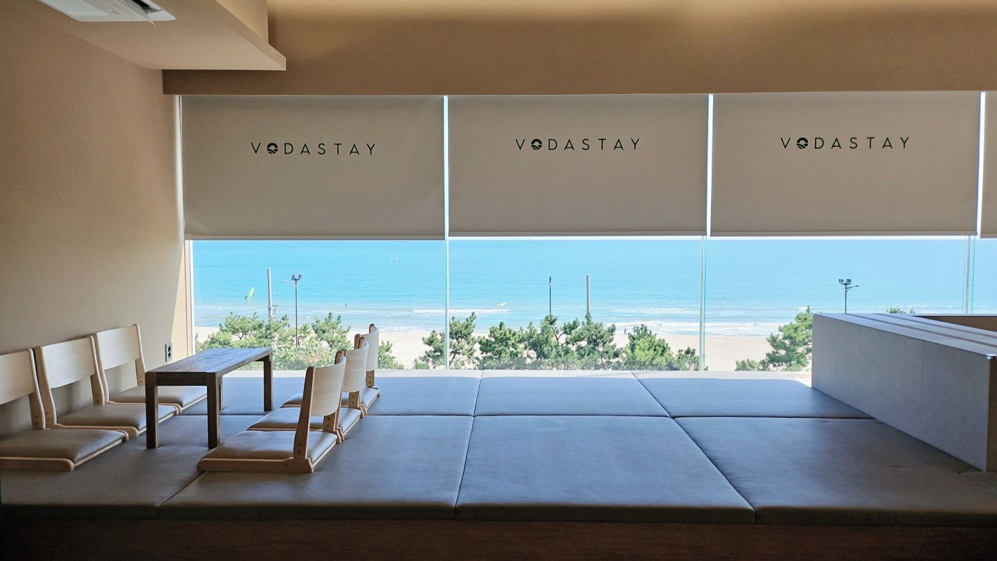 A room with a view of the beach, three 'VODASTAY' signs, a wooden table, and seating.