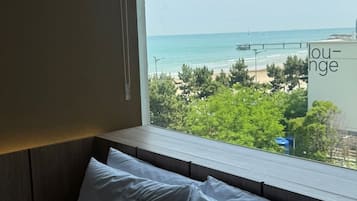 Une chambre d’hôtel avec vue sur la mer, un coin salon et une fenêtre donnant sur la plage et la végétation.