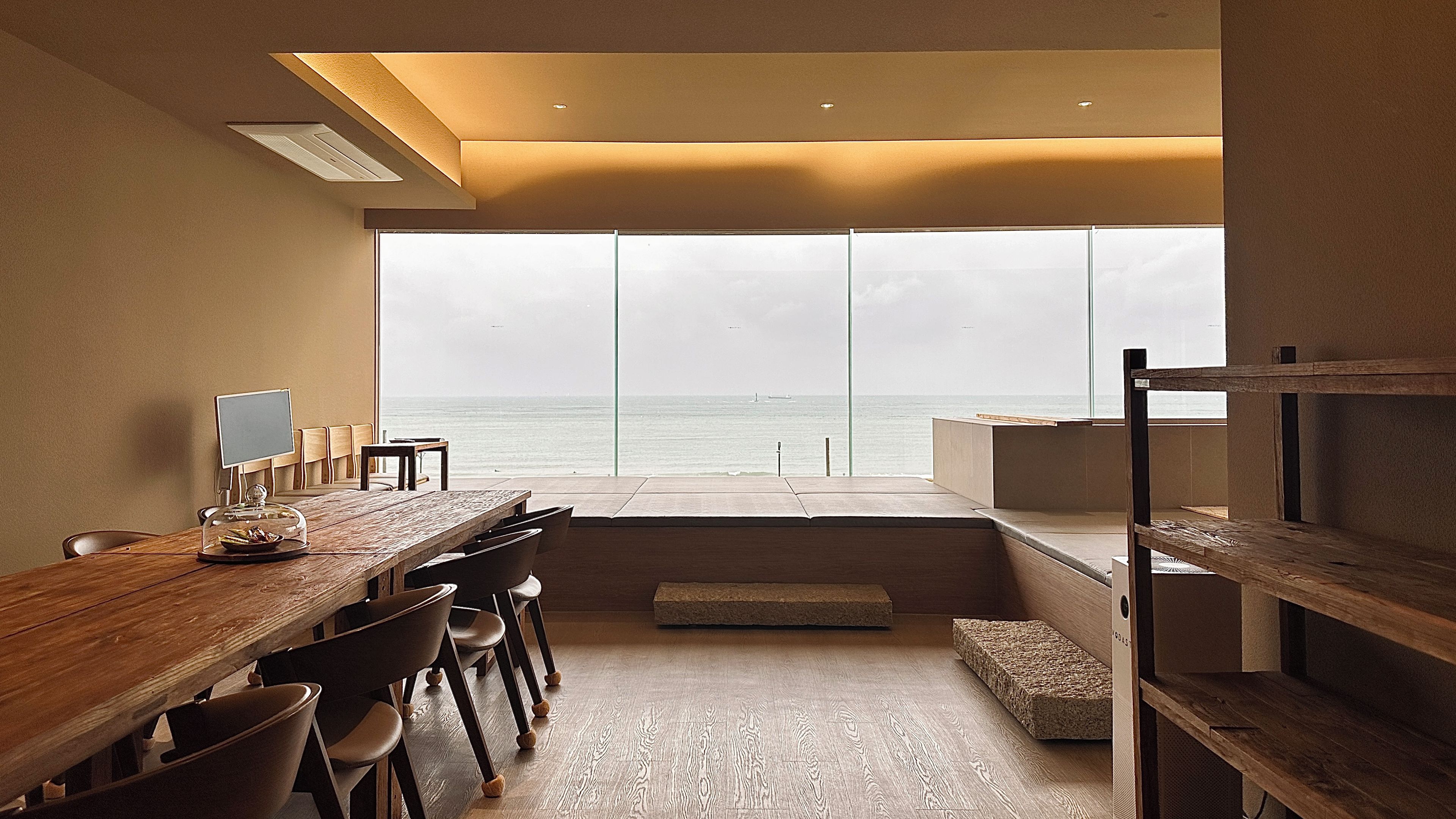 A modern interior with a large window overlooking the sea, a wooden dining table, and a minimalist design.