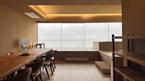 A modern interior with a large window overlooking the sea, a wooden dining table, and a minimalist design. - VODASTAY Songjeong (Busan)