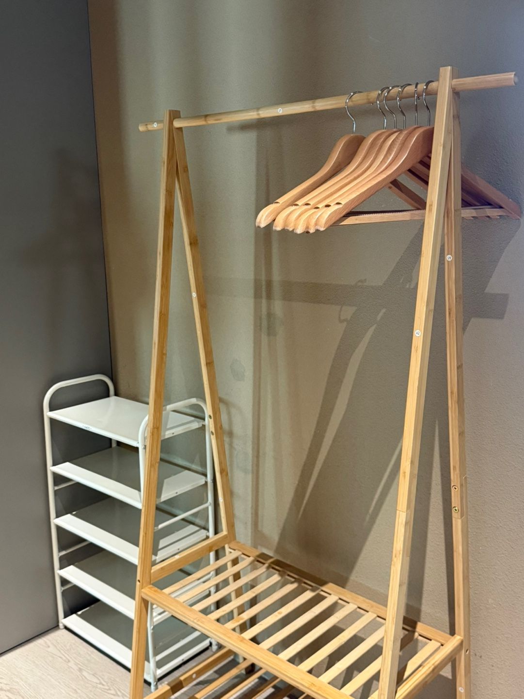 Un armario de madera con barra para colgar y estantes, junto a una estantería metálica blanca.