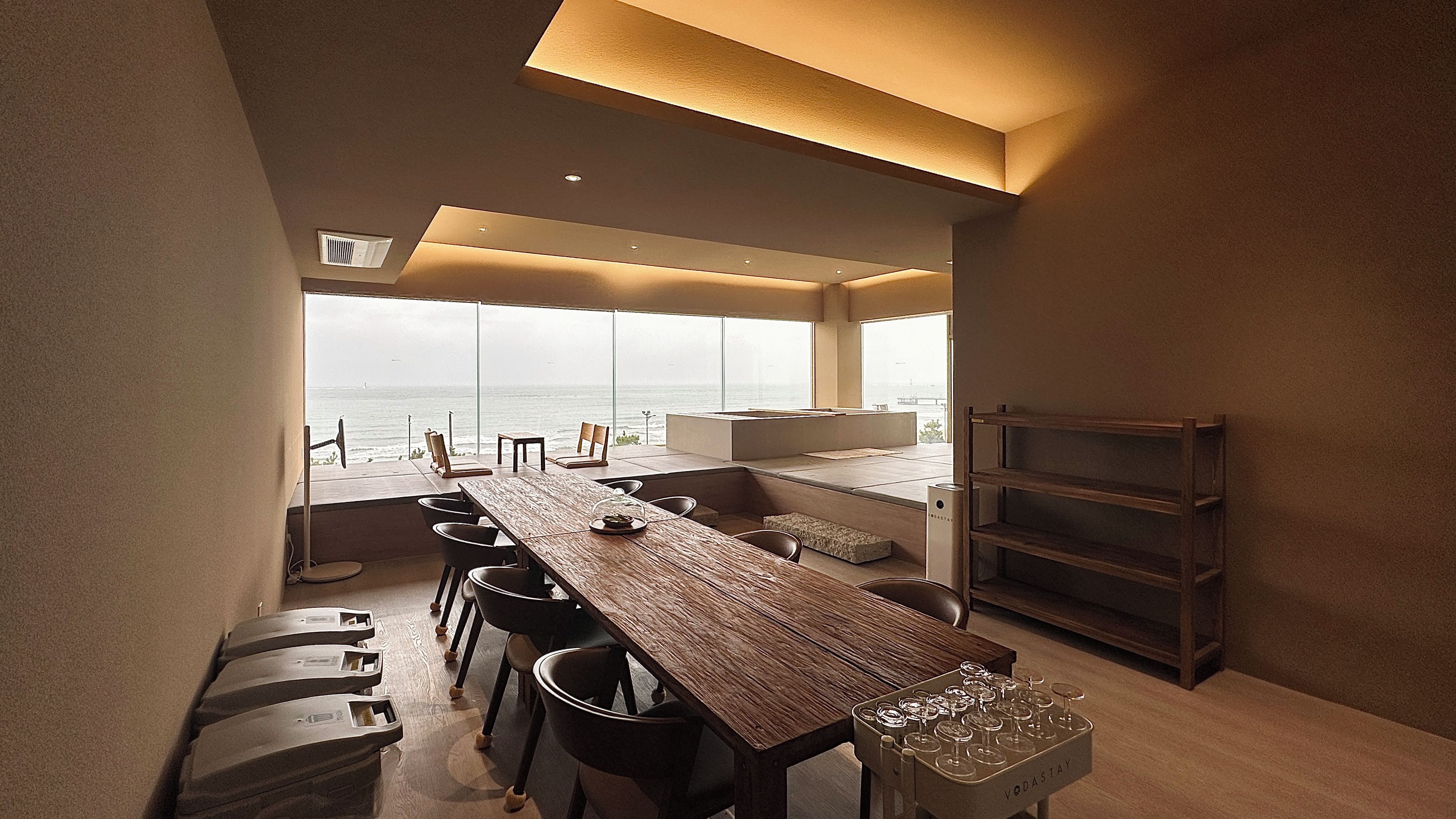 Een moderne keuken met een lange houten tafel, barkrukken en uitzicht op de oceaan.