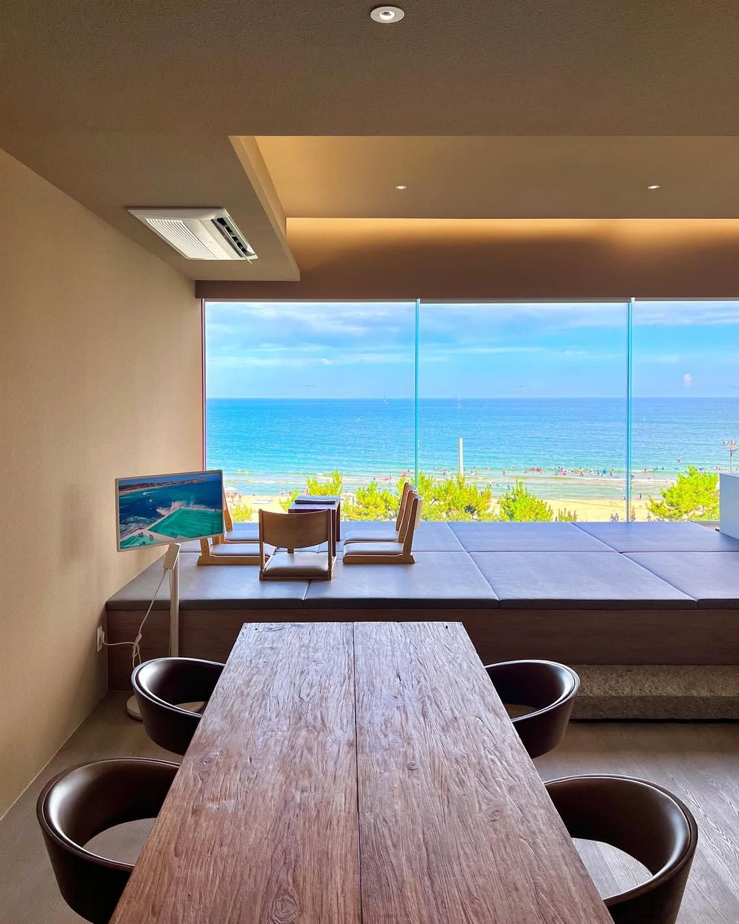 Une chambre moderne avec une grande fenêtre donnant sur une plage, une table en bois et deux chaises.