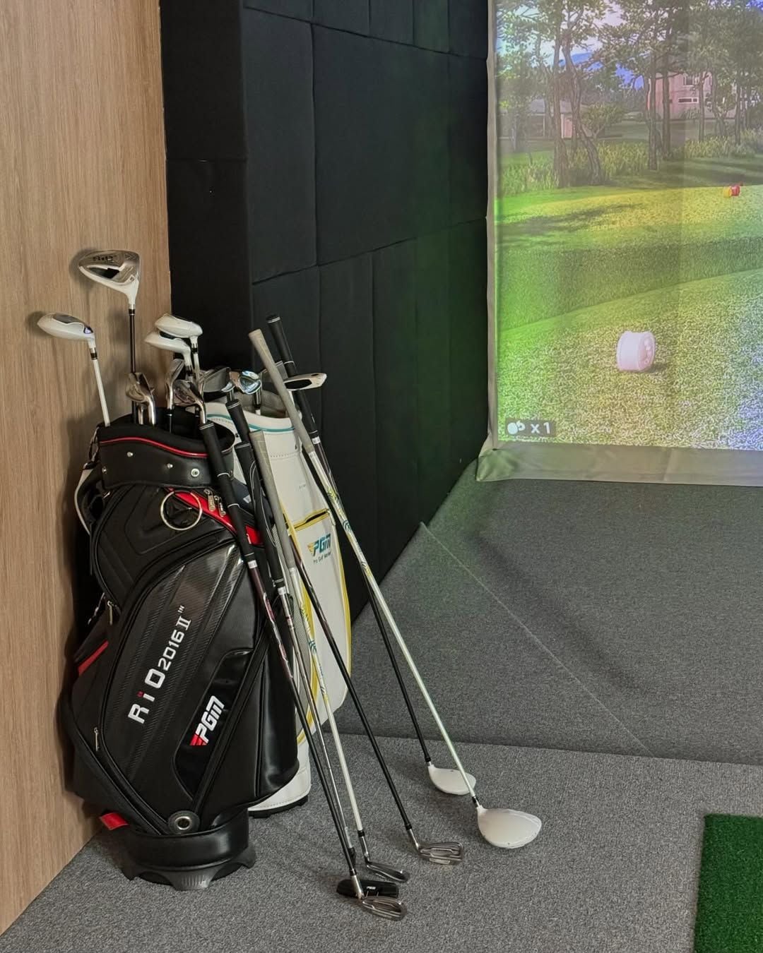 Uma mala de golfe e tacos encostados a uma parede, com um jogo de golfe virtual projetado nela.