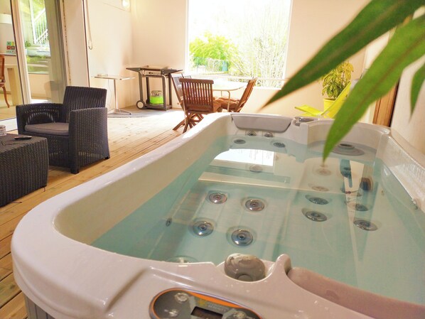 A hot tub with a wooden deck, wicker furniture, and a view of the outdoors. - Vrbo Property (Saint-Amant-Tallende)