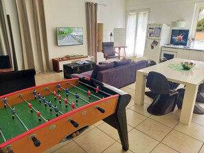 A room with a foosball table, a television, a sofa, a dining table with chairs, and a whiteboard. - Vrbo Property (Saint-Amant-Tallende)