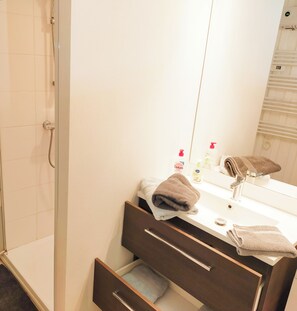 A bathroom with a shower, a sink with a mirror, and a towel rack. - Vrbo Property (Saint-Amant-Tallende)