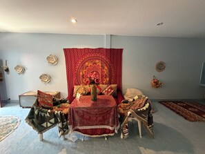 A room with a bed, a table, and a chair, with a tapestry and wall decorations.
