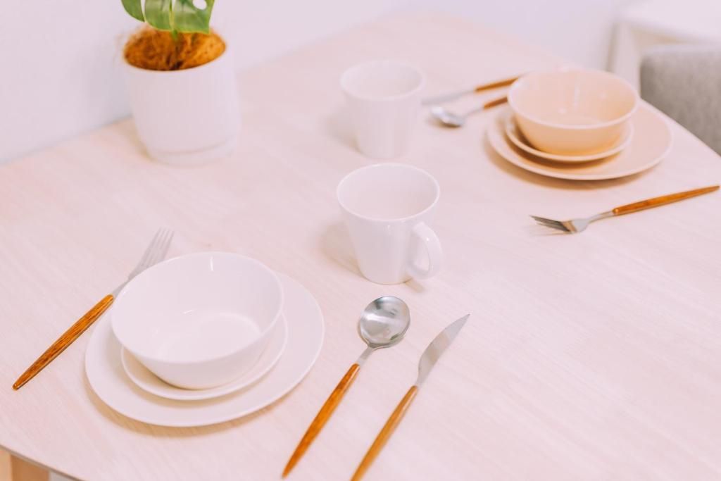 Una mesa de comedor redonda con platos, tazones y cubiertos blancos, incluyendo una cuchara y un cuchillo.