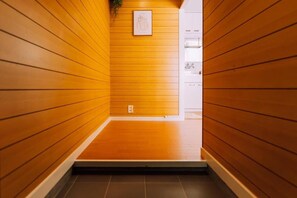 Un estrecho pasillo con paredes de madera y suelo de baldosas que conduce a una habitación con armarios blancos.