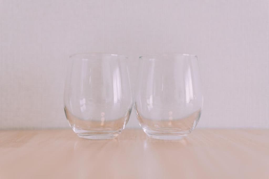 Two clear glass cups on a wooden surface against a plain background.