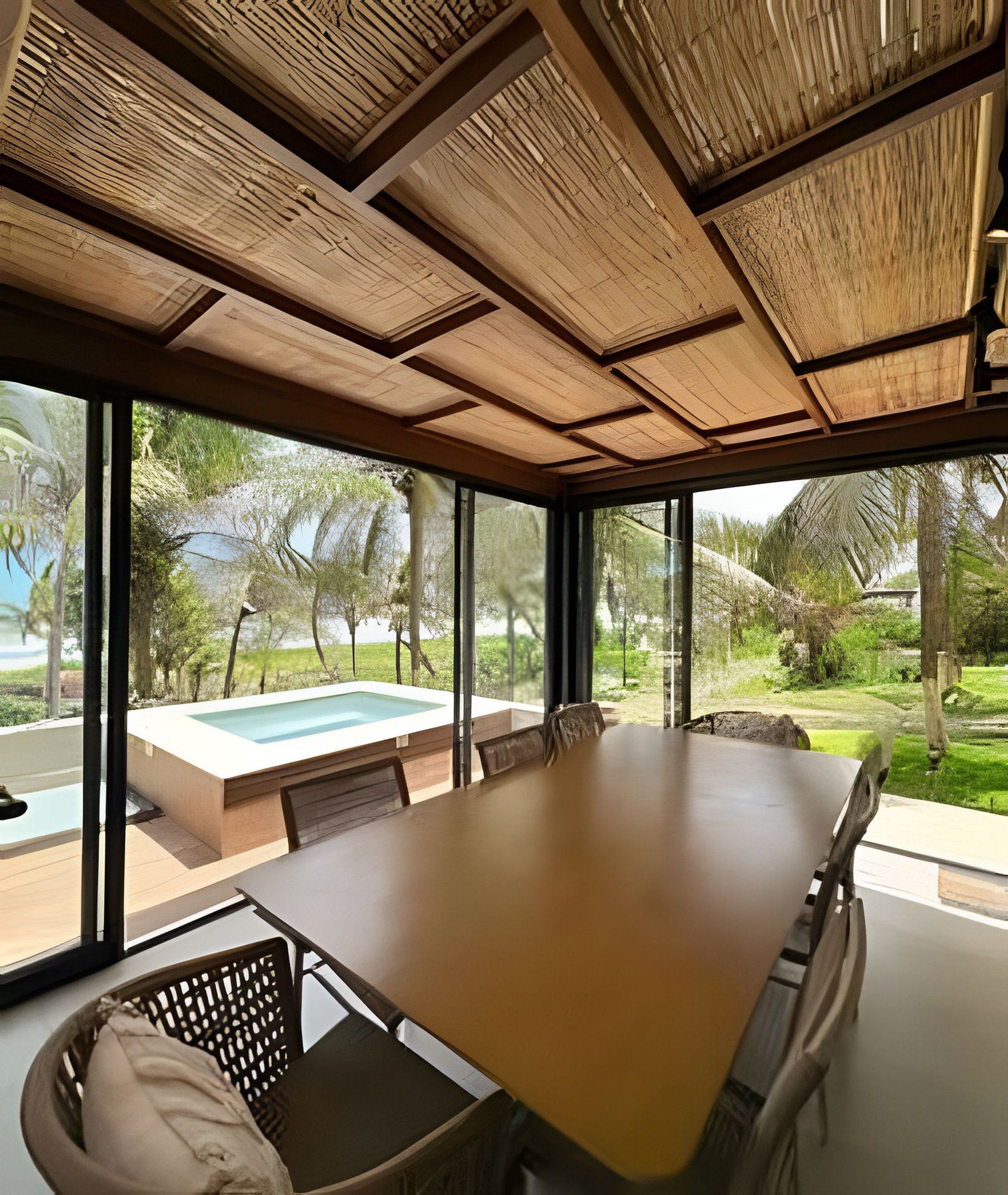 Un comedor moderno con una mesa grande y sillas, amplias ventanas que ofrecen vistas a una piscina y zonas verdes.