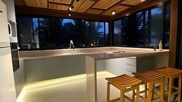 A modern kitchen with a central island, wooden bar stools, and large windows.
