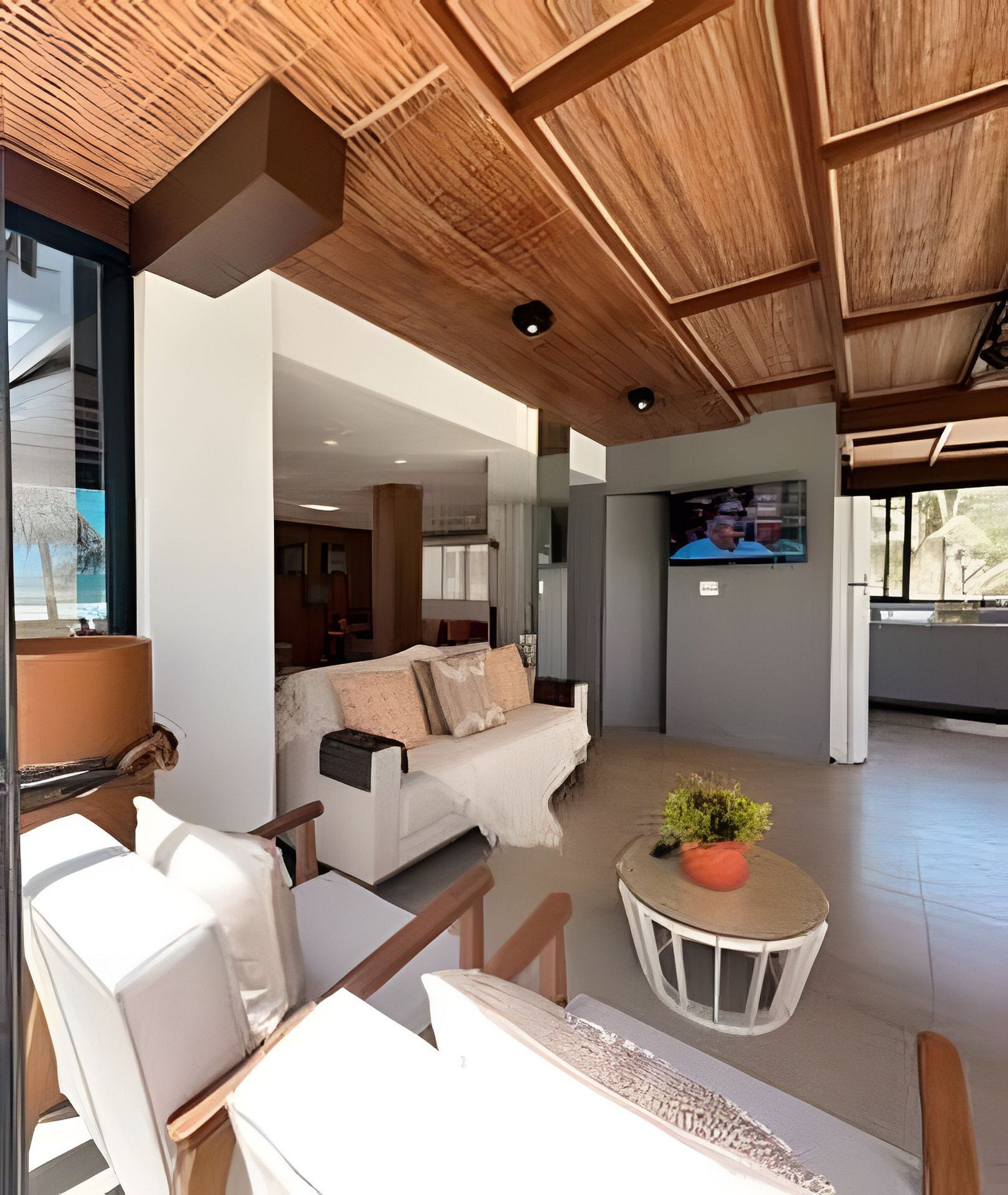 A modern interior with a wooden ceiling, a white sofa, a round table with a plant, and a TV mounted on the wall.
