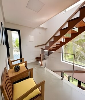 A modern interior with a staircase, a bench, and a view of greenery outside. - casa beira mar guarajuba (Camaçari)