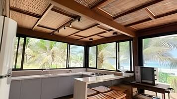 A modern kitchen with a large island, wooden ceiling, and large windows with a view of greenery.