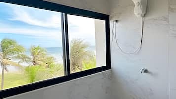 Ein Badezimmer mit großem Fenster, Dusche und Meerblick.