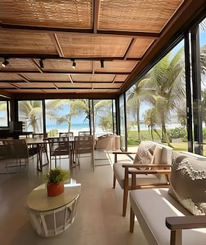 A spacious indoor area with a view of the beach, featuring wooden furniture and a large window.