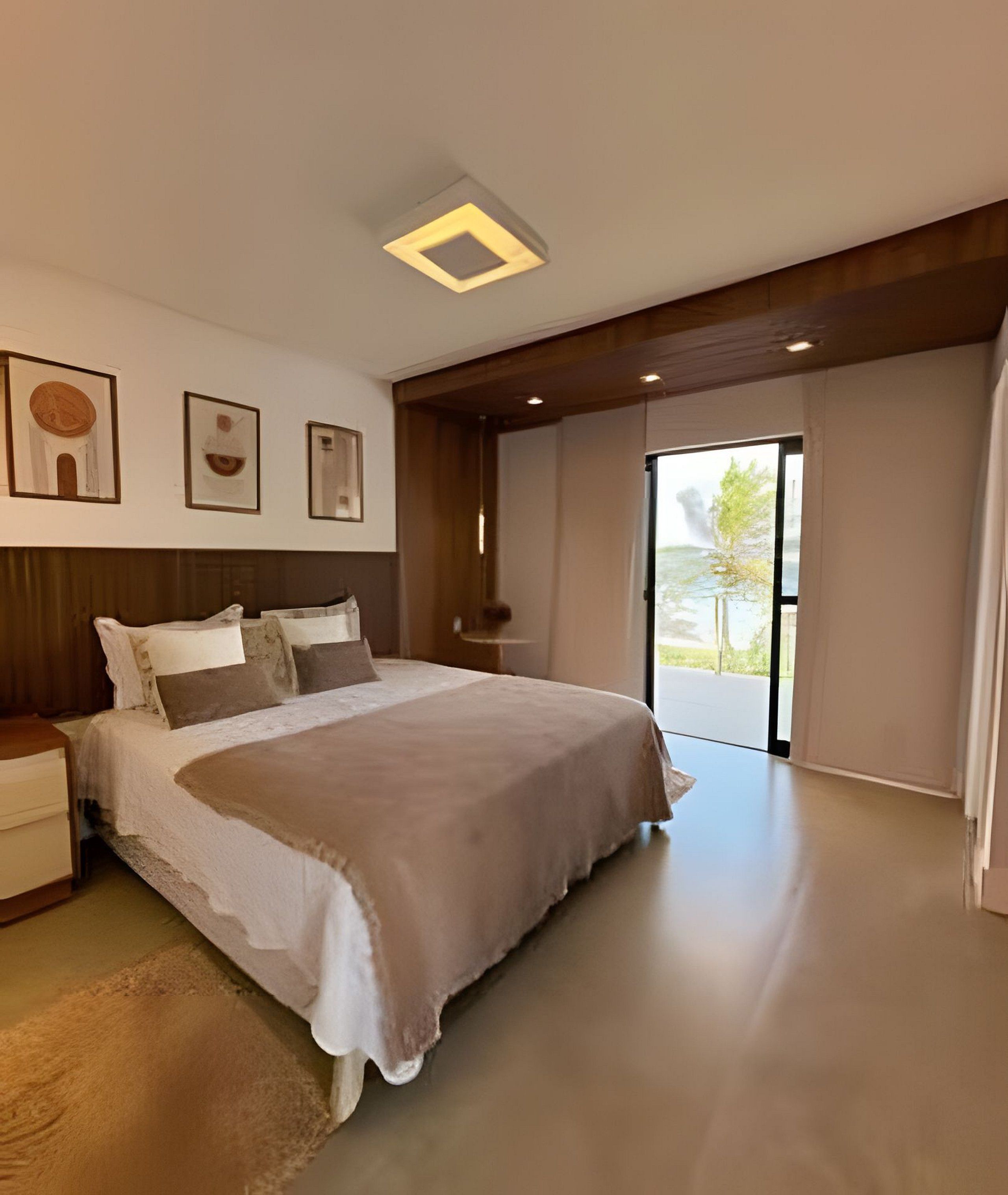 A modern bedroom with a large bed, a nightstand, a bedside table, and a window with a view of greenery.